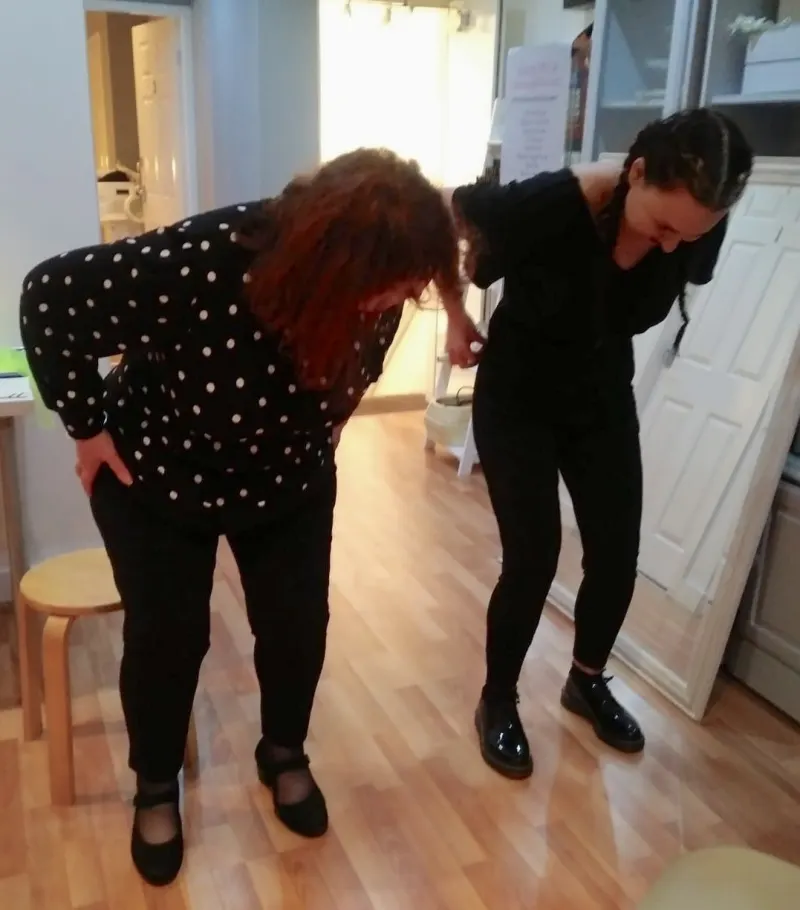 Diane and another woman bending forward together from the hips and knees, exploring a movement side by side.